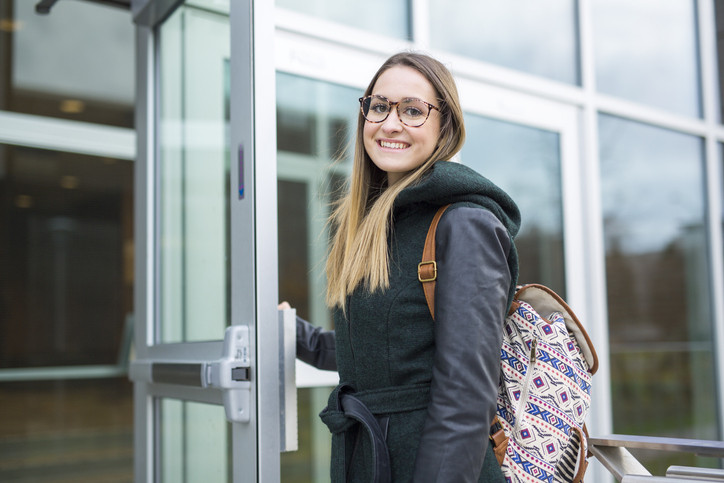 junge Frau mit einem Rucksack vor einem Schulgebäude